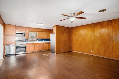 Kitchen with light countertops, dark wood finished floors, stainless steel appliances, wood walls, and a ceiling fan