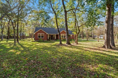 The brick-exterior home is set back from the road under expansive shade from mature trees.