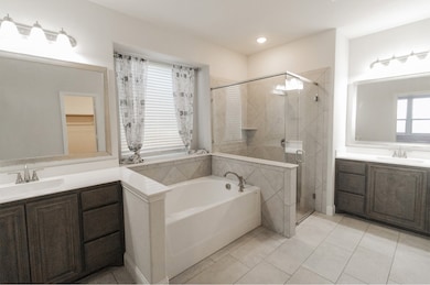 Full bath featuring two vanities, light tile patterned floors, a bath, and a shower stall