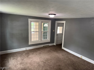 Carpeted empty room featuring a textured ceiling and baseboards