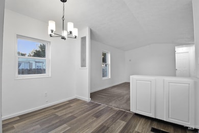 Unfurnished dining area with dark wood-style flooring, lofted ceiling, a chandelier, and a textured ceiling