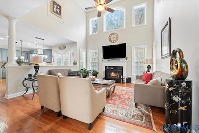 Living room with a high ceiling, light wood finished floors, ornate columns, and a glass covered fireplace