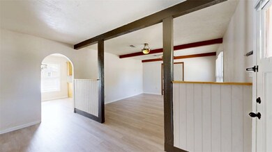 Unfurnished room with light wood finished floors, beam ceiling, and arched walkways