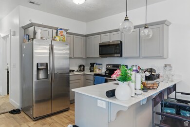Kitchen featuring appliances with stainless steel finishes, gray cabinetry, a kitchen breakfast bar, pendant lighting, and light wood finished floors