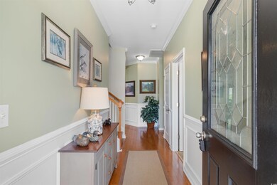 Entrance foyer with crown molding, wood finished floors, a wainscoted wall, stairs, and a decorative wall