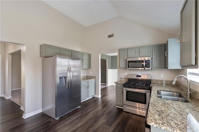 Kitchen with appliances with stainless steel finishes, light stone counters, dark wood-style flooring, and high vaulted ceiling