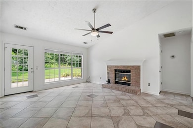 Unfurnished living room featuring ceiling fan, a textured ceiling, vaulted ceiling, a fireplace, and light tile patterned floors