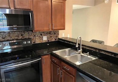Kitchen with appliances with stainless steel finishes, dark stone counters, brown cabinets, and tasteful backsplash