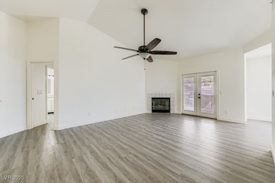 Unfurnished living room featuring light wood-type flooring, a tiled fireplace, high vaulted ceiling, a ceiling fan, and french doors