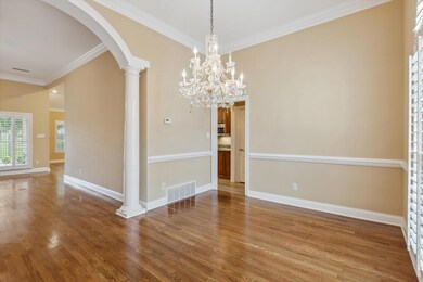 Dining room with arched walkways, crown molding, wood finished floors, baseboards, and decorative columns