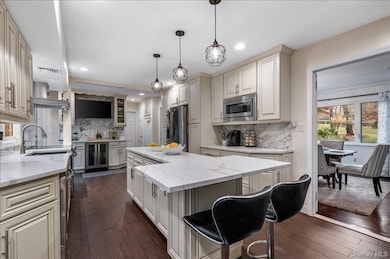 Kitchen featuring cream cabinets, light stone counters, hanging light fixtures, dark wood-style flooring, and a kitchen breakfast bar