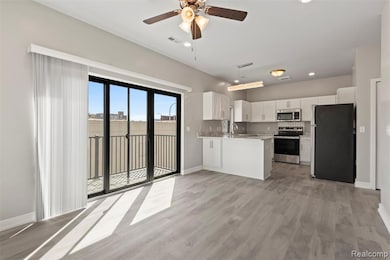 Kitchen with stainless steel appliances, white cabinets, open floor plan, light wood finished floors, and a peninsula