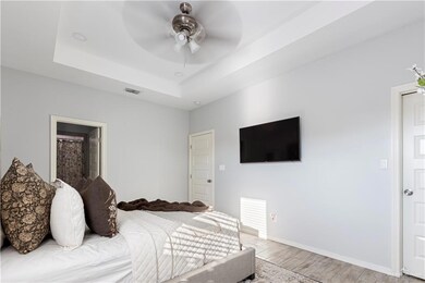 Bedroom featuring light wood-style flooring, a tray ceiling, baseboards, and ceiling fan