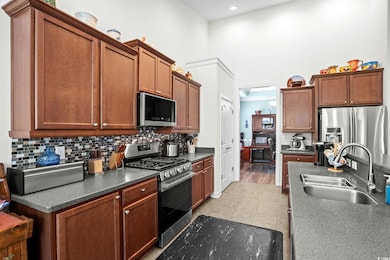Kitchen with stainless steel appliances, brown cabinets, backsplash, a towering ceiling, and light tile patterned floors