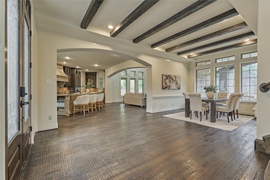 This inviting home features an open-concept layout with a seamless flow from a spacious kitchen to the dining and living areas. The room is adorned with elegant dark wood beams, large windows providing ample natural light, and stylish finishes, creating a warm and welcoming atmosphere.