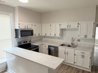 Kitchen featuring appliances with stainless steel finishes, a sink, dark wood finished floors, white cabinets, and a textured ceiling