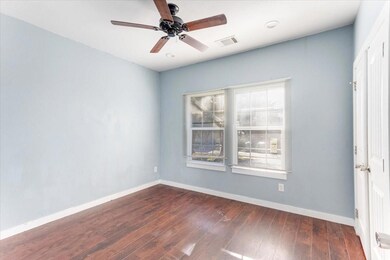 Empty room with dark wood-style floors, ceiling fan, visible vents, and baseboards