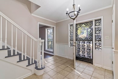 Foyer entrance featuring a textured ceiling, a chandelier, crown molding, stairs, and a decorative wall