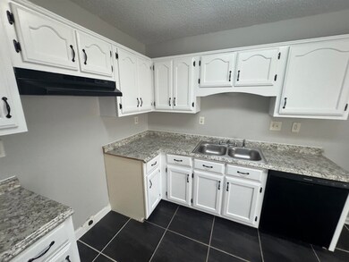 Kitchen with a sink, black dishwasher, under cabinet range hood, white cabinetry, and a textured ceiling