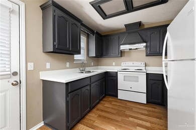 Kitchen with range hood, sink, light hardwood / wood-style floors, and white appliances