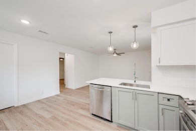 Kitchen featuring a peninsula, stainless steel appliances, light wood-type flooring, hanging light fixtures, and backsplash