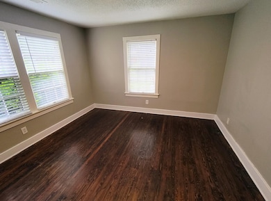 Spare room featuring dark wood-style flooring, a textured ceiling, and baseboards