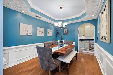 Dining room with a decorative wall, wainscoting, a tray ceiling, arched walkways, and crown molding