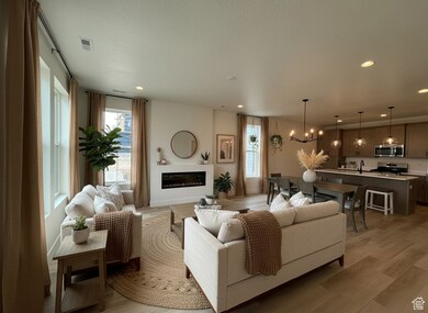 Living area with a chandelier, a glass covered fireplace, light wood finished floors, recessed lighting, and healthy amount of natural light