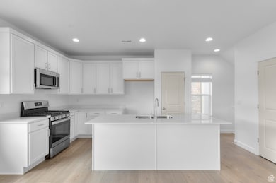 Kitchen with stainless steel appliances, white cabinets, recessed lighting, light wood-type flooring, and a center island with sink
