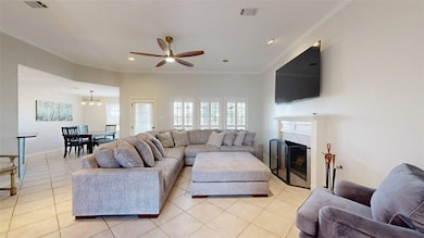 Living room featuring crown molding, plenty of natural light, light tile patterned flooring, a ceiling fan, and a tiled fireplace