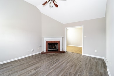Unfurnished living room featuring wood finished floors, a fireplace, vaulted ceiling, and a ceiling fan