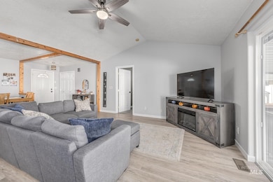 Living area featuring a textured ceiling, light wood-style flooring, ceiling fan, and vaulted ceiling