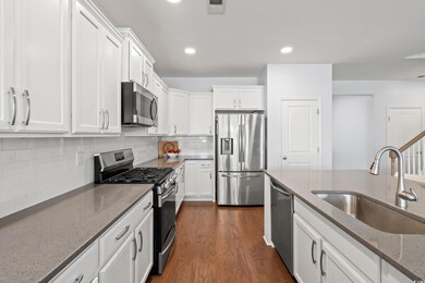 Kitchen featuring stainless steel appliances, white cabinets, light stone countertops, dark wood finished floors, and decorative backsplash
