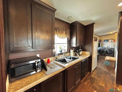 Kitchen featuring light countertops, dark brown cabinetry, dark wood-type flooring, stainless steel microwave, and washing machine and dryer