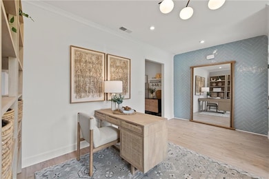Home office with an accent wall, wood finished floors, wallpapered walls, crown molding, and baseboards