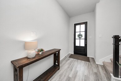 Bright and welcoming entryway with light flooring and a modern black door.  Stairs with carpeted steps lead upwards, creating an inviting atmosphere.