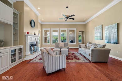 Living room with ceiling fan, dark wood finished floors, arched walkways, a high end fireplace, and ornamental molding