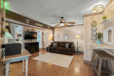 Living room featuring wooden walls, a wall mounted AC, wood finished floors, ceiling fan, and a textured ceiling