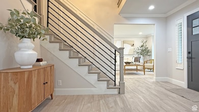Foyer entrance featuring light wood-style floors, crown molding, recessed lighting, stairway, and plenty of natural light