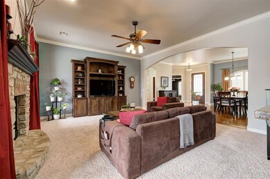 Living area with baseboards, carpet floors, a stone fireplace, arched walkways, and a ceiling fan