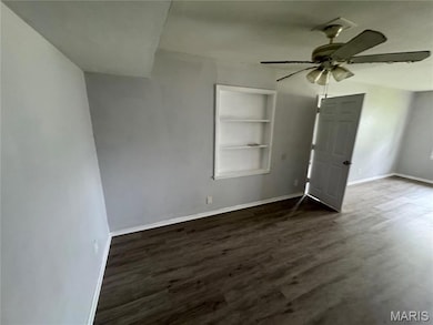 Unfurnished room with built in features, dark wood-type flooring, and a ceiling fan
