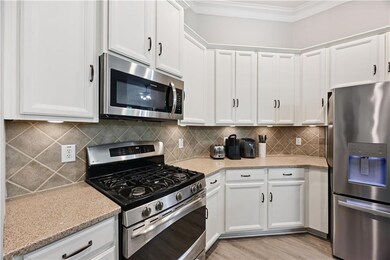 Kitchen featuring stainless steel appliances, ornamental molding, white cabinetry, light wood-style floors, and light stone counters