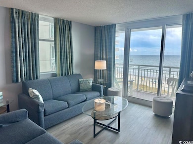 Living room featuring view of water and beach, wood finished floors, and a textured ceiling