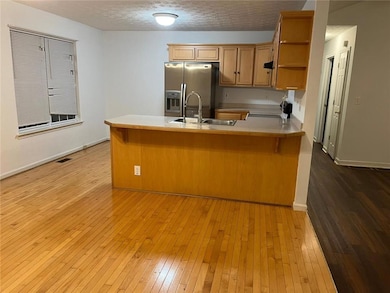 Kitchen with open shelves, light wood-type flooring, light countertops, stainless steel fridge, and a textured ceiling