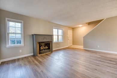 Unfurnished living room with a textured ceiling, wood finished floors, a fireplace, and baseboards