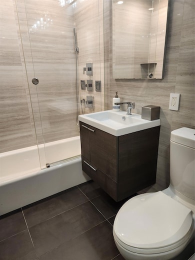 Bathroom featuring tile patterned floors, enclosed tub / shower combo, tile walls, and toilet
