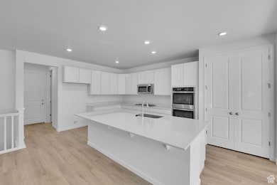 Kitchen with white cabinetry, an island with sink, light wood finished floors, recessed lighting, and appliances with stainless steel finishes