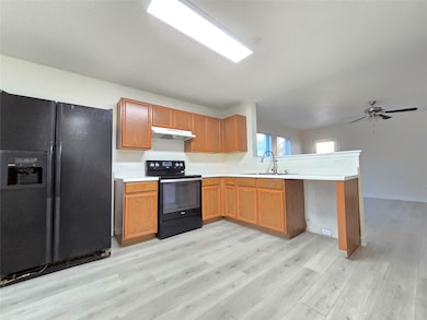 Kitchen featuring black appliances, a peninsula, light countertops, and brown cabinetry