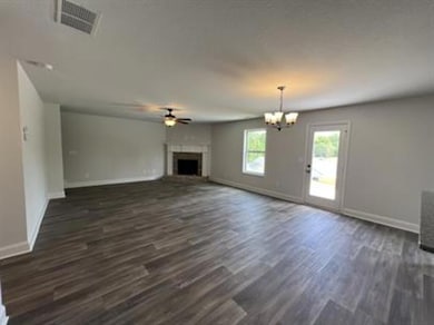 Unfurnished living room featuring dark wood-style flooring, a fireplace with raised hearth, a ceiling fan, and a chandelier
