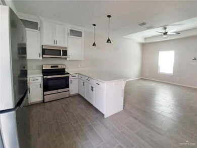 Kitchen featuring appliances with stainless steel finishes, white cabinets, light countertops, a peninsula, and pendant lighting